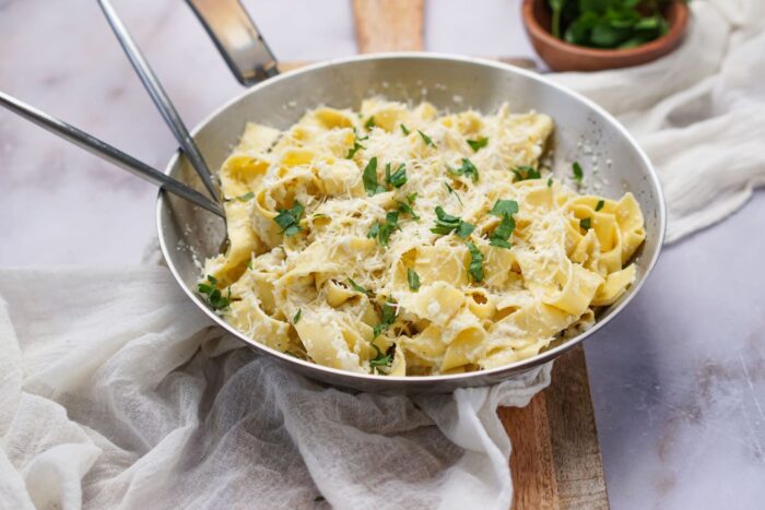 Creamy cauliflower alfredo sauce in a skillet on a wood board.