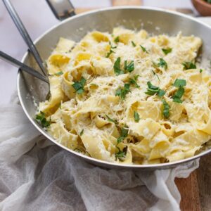 A saute pan filled with fettuccine and cauliflower alfredo sauce garnished with parsley.