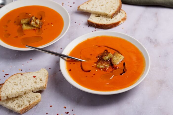 Two generous bowls of healthy tomato soup recipe in shallow white bowls, drizzled with olive oil. 