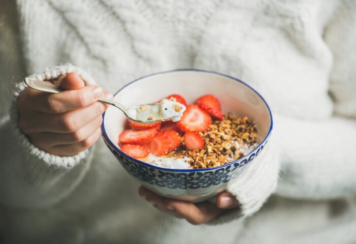 Woman holding bowl of oatmeal topped with greek yogurt and strawberries.