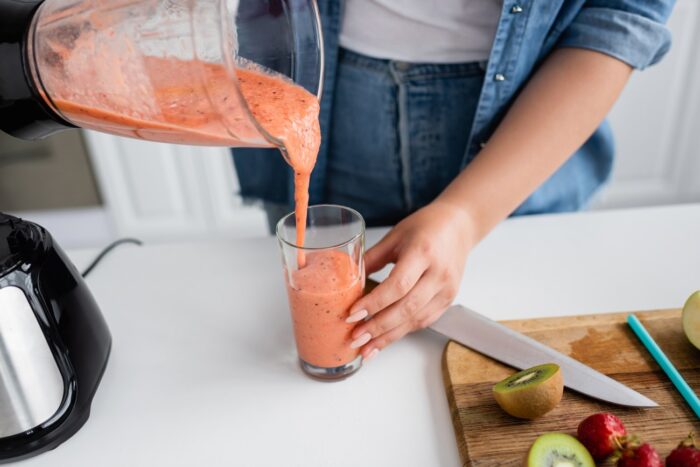 Woman pouring orange smoothie into glass for small changes for weight loss.