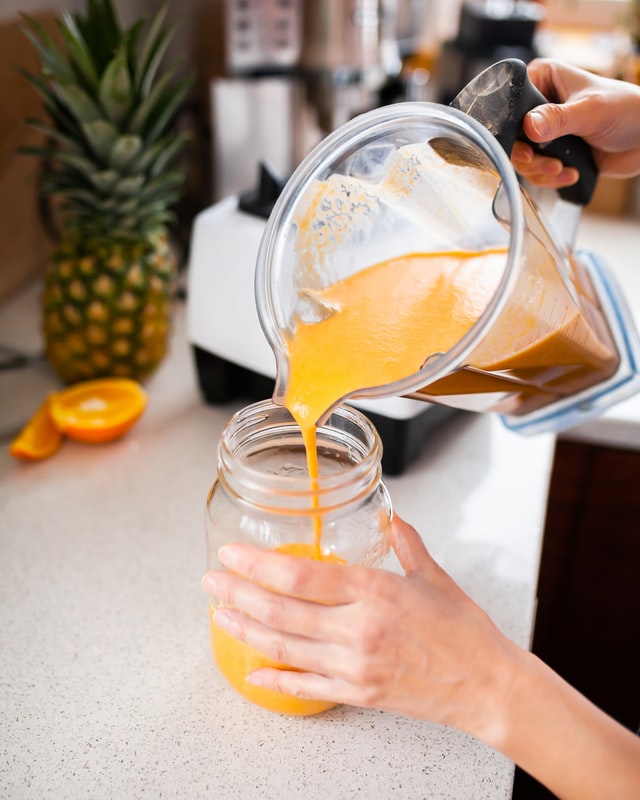 Women pouring blended orange smoothie into glass.