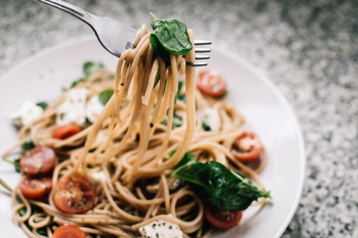 Whole wheat pasta with tomatoes and basil on a white plate. 